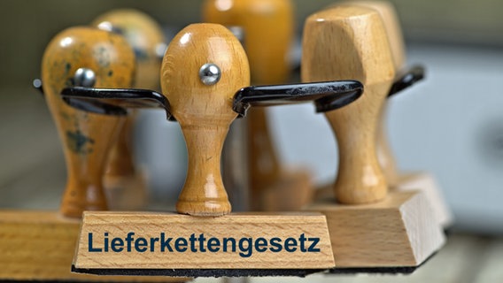 Ein Holzstempel mit der Aufschrift "Lieferkettengesetz" sowie weitere Stempel in einem Stempelkarussell stehen auf einem Schreibtisch. © SULUPRESS.DE Foto: Torsten Sukrow