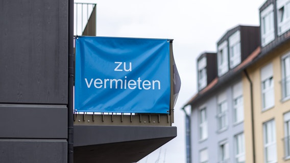"Zu vermieten" steht auf einer Plane, die an einem Balkon-Geländer einer Neubau-Wohnung angebracht ist. © picture alliance Foto: Daniel Karmann