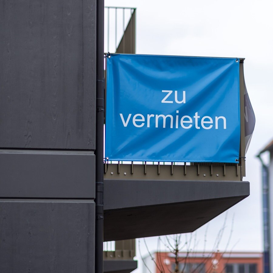 "Zu vermieten" steht auf einer Plane, die an einem Balkon-Geländer einer Neubau-Wohnung angebracht ist. © picture alliance Foto: Daniel Karmann