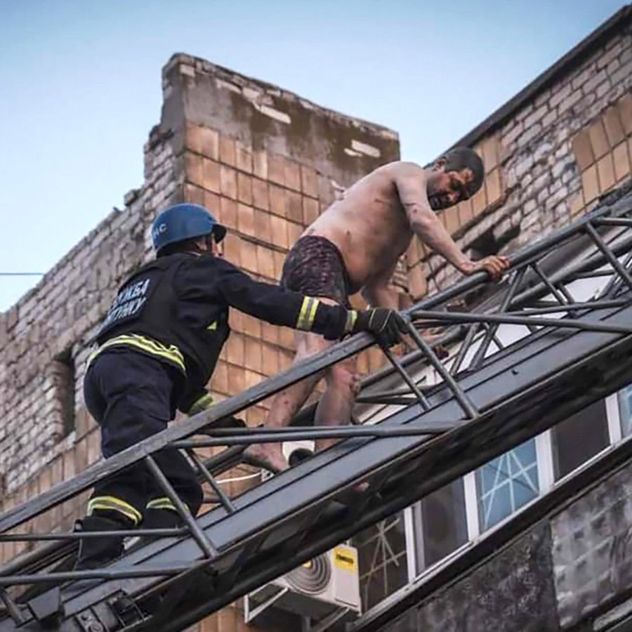 Ukrainische Rettungskräfte vom Katastrophenschutz retten Menschen aus einem beschädigten Gebäude nach Raketeneinschlägen. © AP Foto: Evgeniy Maloletka