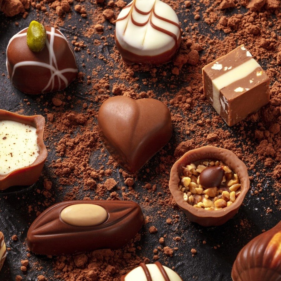 Eine Auswahl von Schokoladen-Pralinen liegt auf einem mit Kakao gepudertem Untergrund © Picture Alliance / / Zoonar | Katerina Solovyeva Foto: Katerina Solovyeva