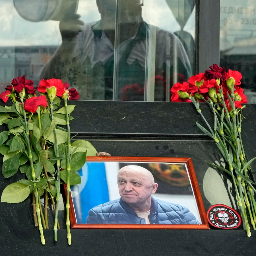 Ein Porträtbild des russischen Söldnerführers, Jewgeni Prigoschin, steht an einer informellen Gedenkstätte vor einem Café in St. Petersburg (Russland), das im Besitz von Prigoschins Firma ist. © AP/dpa Foto: Dmitri Lovetsky