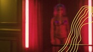Eine Prostituierte steht in Unterwäsche in einem rot ausgeleuchtetem Türrahmen und wartet auf einen Freier. © picture alliance Foto: Robin Utrecht