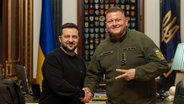 Wolodymyr Selenskyj und Walerij Saluschnyj schütteln sich die Hände. © picture alliance 
