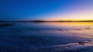 Ein vereister Strand mit Sonnenaufgang am Horizont. © picture alliance Foto: Torsten Sukrow