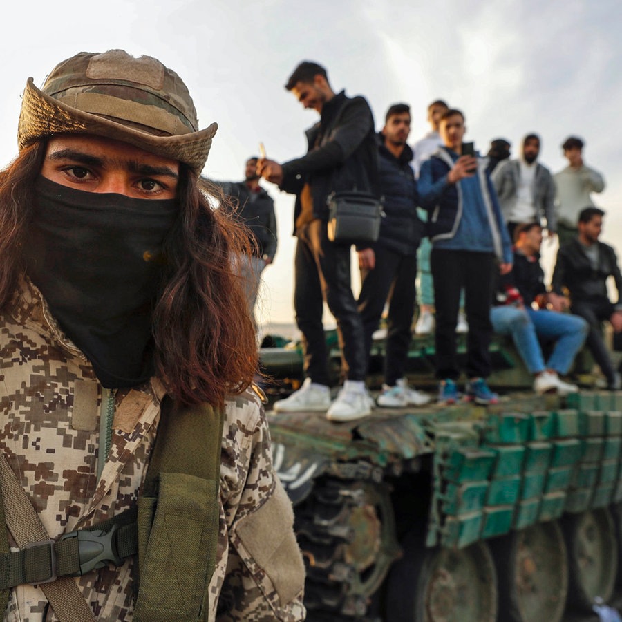Ein syrischer Oppositionskämpfer (links) hält Wache, während syrische Bürger auf einem Panzer der Regierungstruppen stehen, der durch die Aufständischen auf der Straße in Damaskus abgestellt wurde. © AP Foto: Omar Sanadiki