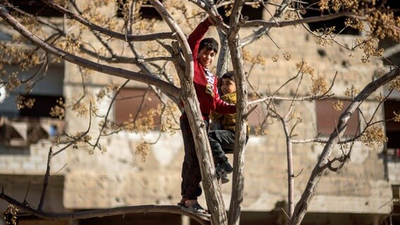 Kinder spielen in einem Baum in der Stadt Harasta, die während des Krieges zwischen Oppositionskräften und dem Assad-Regime heftig umkämpft war, am Stadtrand von Damaskus (Syrien). © AP/dpa Foto: Mosa'ab Elshamy