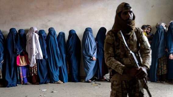 Ein Taliban-Kämpfer steht Wache, während Frauen darauf warten, Lebensmittelrationen zu erhalten, die von einer humanitären Hilfsorganisation in Kabul, Afghanistan, verteilt werden, Dienstag, 23. Mai 2023. © picture alliance Foto: Ebrahim Noroozi