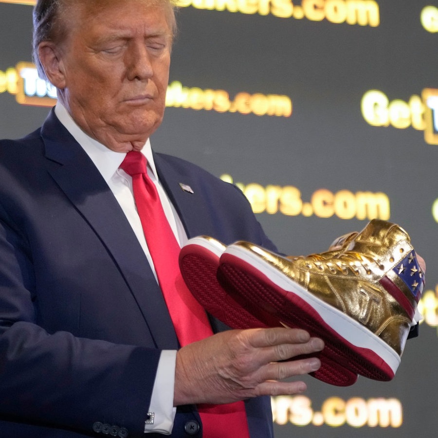 Der republikanische Präsidentschaftskandidat Donald Trump hält goldene Trump-Sneakers auf der
Sneaker Con Philadelphia in Händen. © picture alliance Foto: Manuel Balce