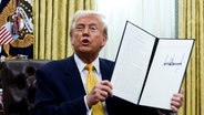 US-Präsident Donald Trump hält eine unterzeichnete Durchführungsverordnung im Oval Office des Weißen Hauses. © picture alliance/dpa/Pool | Uncredited 