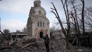 Ein ukrainischer Soldat fotografiert eine beschädigte Kirche nach einem Bombenangriff in der Ukraine. © picture alliance/dpa/AP Foto: Evgeniy Maloletka
