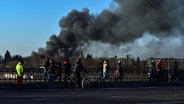 Menschen laufen über eine Straße, im Hintergrund ist eine Rauchwolke zu sehen © dpa/IHA/AP Foto: Ismail Coskun