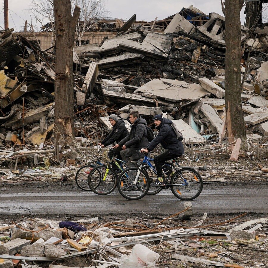 Drei Männer fahren auf ihren Fahrrädern an zerstörten Gebäuden vorbei © picture alliance/dpa/AP | Vadim Ghirda Foto:  Vadim Ghirda