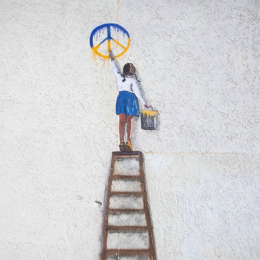 Ein Kunstwerk des italinischen Street-Art Künstlers Salvatore Benintende Tvboy in Butcha zeigt ein Mädchen auf einer Leiter, das ein blau-gelbes Peace-Zeichen an die Wand malt. © picture alliance Foto: Oleksii Chumachenko