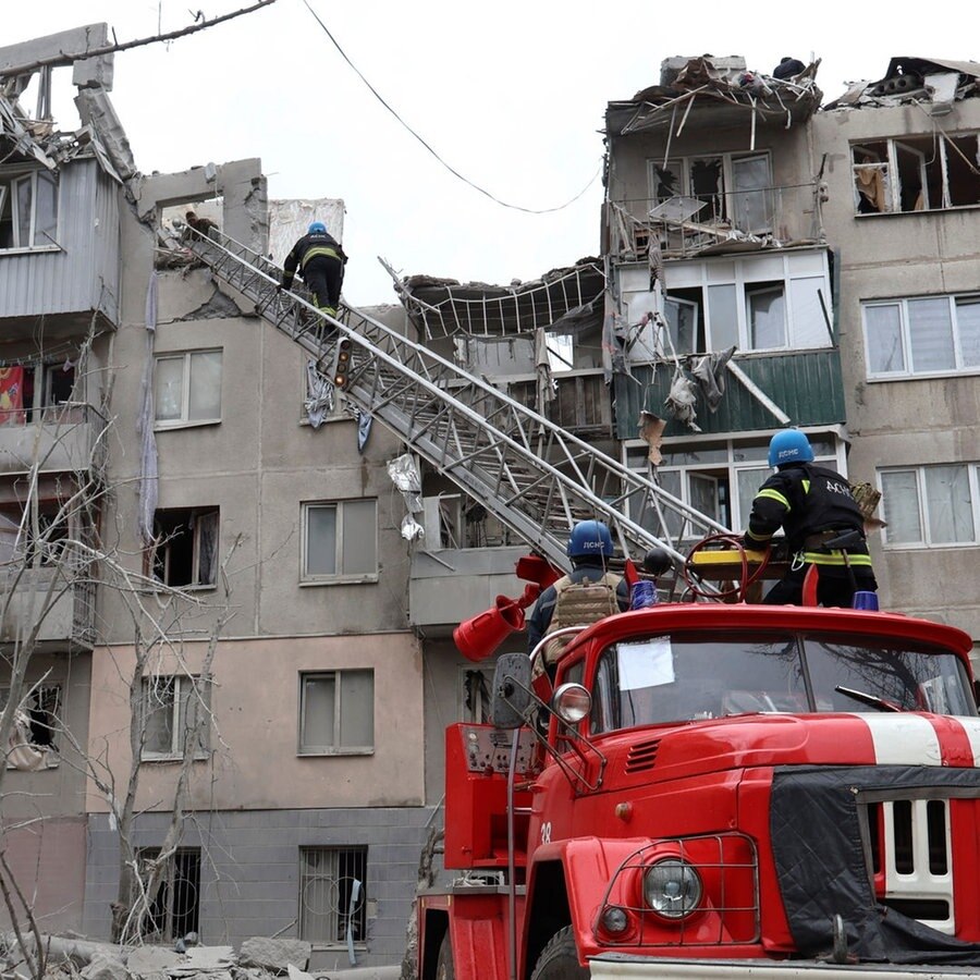 Feuerwehrleute arbeiten daran, ein Feuer zu löschen, während sie nach einem Raketenangriff nach möglichen Opfern suchen. © picture alliance/dpa/AP Foto: Roman Chop