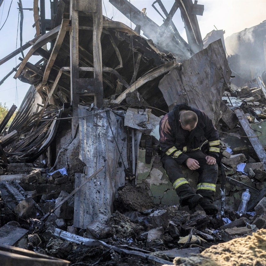 Ein ukrainischer Feuerwehrmann sitzt auf einem Trümmerhaufen eines durch einen russischen Angriff zerstörten Gebäudes. © picture alliance / abaca | Smoliyenko Dmytro/Ukrinform/ABACA 