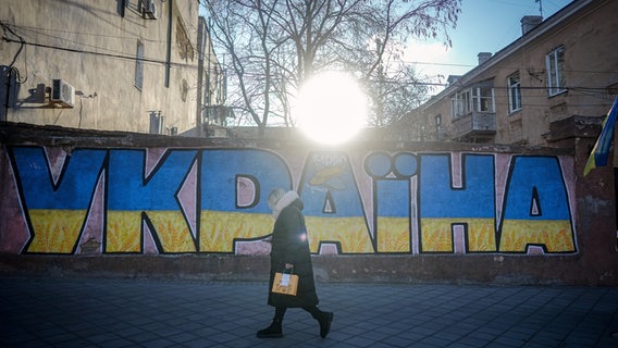 Eine Frau geht an einem Ukraine Graffiti in der Hafenstadt vorbei. Am 24. Februar 2024 jährt sich der Beginn des russischen Angriffskrieges gegen die Ukraine zum zweiten Mal. © picture alliance/dpa Foto: Kay Nietfeld