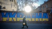 Eine Frau geht an einem Ukraine Graffiti in der Hafenstadt vorbei. Am 24. Februar 2024 jährt sich der Beginn des russischen Angriffskrieges gegen die Ukraine zum zweiten Mal. © picture alliance/dpa Foto: Kay Nietfeld