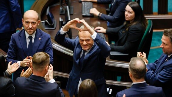 Donald Tusk (Mitte) formt nach seiner Wahl zum polnischen Premierminister im Parlament ein Herz mit seinen Händen. © AP/dpa-Bildfunk Foto: Michal Dyjuk/