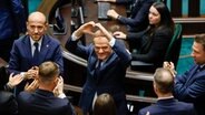 Donald Tusk (Mitte) formt nach seiner Wahl zum polnischen Premierminister im Parlament ein Herz mit seinen Händen. © AP/dpa-Bildfunk Foto: Michal Dyjuk/