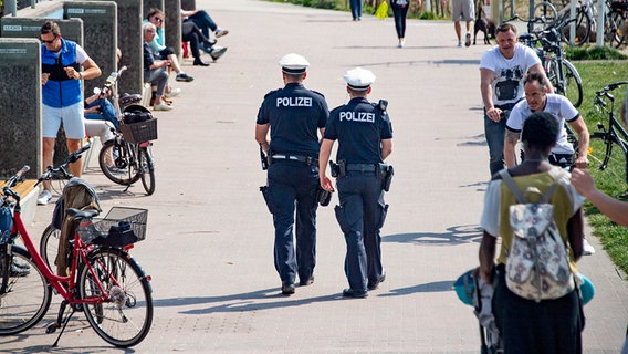 Zwei Polizisten gehen zu Fuß auf einem Spazierweg und kontrollieren Fußgänger und Radfahrer an einem sonnigen Tag. © dpa bildfunk Foto: Axel Heimken
