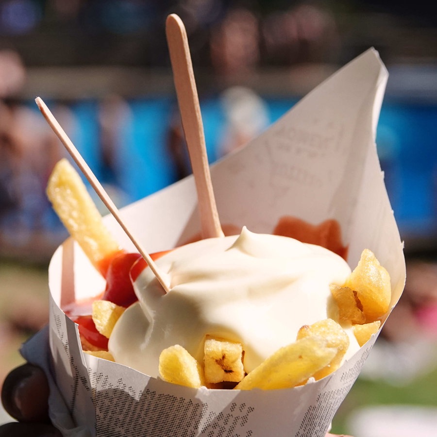 Ein Badegast in einem Freibad hält eine Portion Pommes Frites mit Ketchup und Mayonnaise in der Hand © picture alliance/dpa Foto: Julian Weber