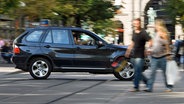 Ein BMW X5-Geländewagen fährt auf einer Straße an Fußgängern vorbei. © dpa picture alliance Foto: Gaetan Bally