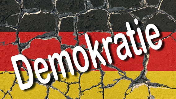 Das Wort Demokratie steht auf einer brüchigen Mauer in schwarz-rot-goldenen Hintergrund (Fotocollage). © Imago/Ralph Peters 