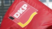Eine rote Fahne mit dem Logo der Deutschen Kommunistischen Partei (DKP) über den Deutschland-Farben Schwarz, Rot, Gold liegend. © picture alliance/imageBROKER Foto: Dirk Enters