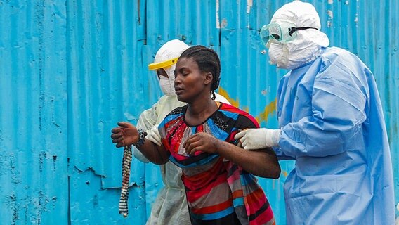 Mediziner in Schutzanzügen begleiten in Liberia eine Frau, die mutmaßlich an Ebola erkrankt ist. © dpa bildfunk Foto: Ahmed Jallanzo