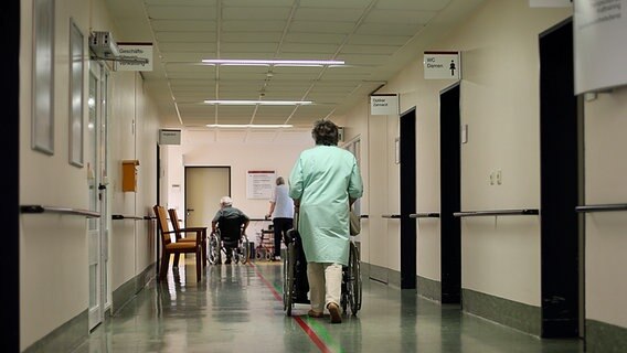 Eine Frau schiebt einen Rollstuhl über einen Krankenhausflur. © picture alliance/dpa Foto: Christian Charisius