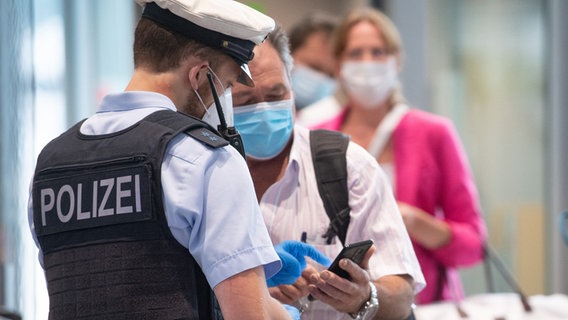 Bei der Einreise an einem Flughafen kontrolliert ein Polizeibeamter das Corona-Zertifikat von einem Passagier. © picture alliance/dpa Foto: Boris Roessler