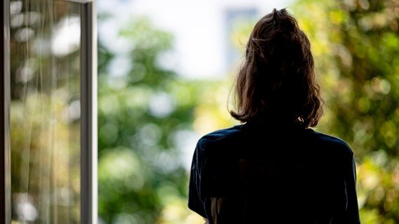 Eine Frau steht in ihrer Wohnung an einem Fenster. © dpa Foto: Fabian Sommer