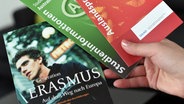 Eine Studentin hält ein Buch über das Erasmus-Programm und Informationsbroschüren über Auslandspraktika in den Händen. © picture alliance/dpa Foto: Jens Kalaene