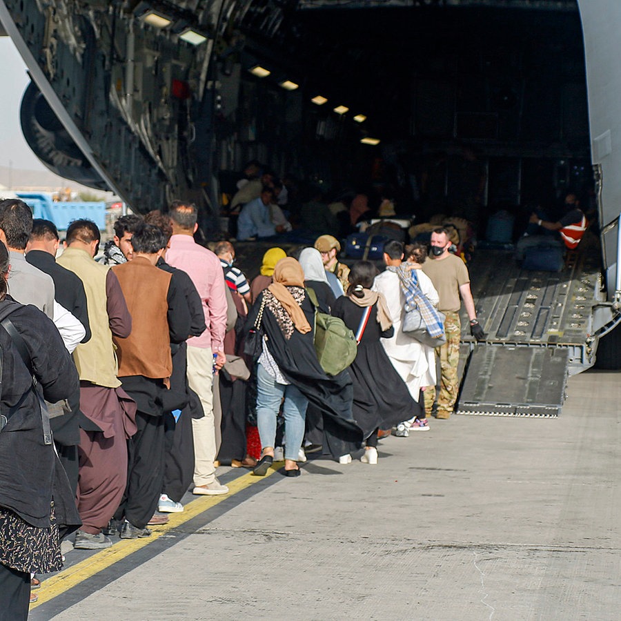 Menschen stehen auf dem Rollfeld und gehen an Bord eines US-Transportflugzeugs von Typ C-17 Globemaster III während ihrer Evakuierung am Hamid Karzai International Airport in Afghanistan. © U.S. Marines/ZUMA Press Wire Service/dpa 