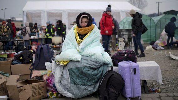 A woman covers herself with a blanket to keep warm after fleeing Ukraine and arriving at the border crossing in Medyka, Poland.  © picture alliance / dpa / AP Photo: Markus Schreiber