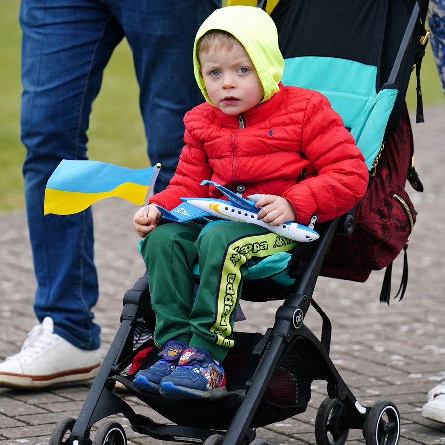 Ein Kind sitzt in einem Kinderwagen und hält eine ukrainische Flagge in der Hand. © picture alliance/empics Foto: Mike Egerton