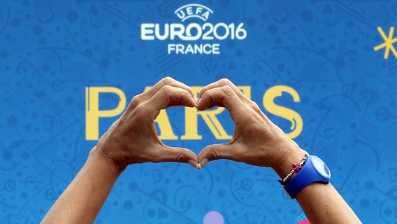 Zwei Hände formen ein Herz vor einem Plakat der Fußball-Europameisterschaft in Frankreich. © dpa bildfunk Foto: Abedin Taherkenareh