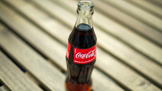 Eine Coca-Cola-Glasflasche steh auf einem Holztisch. © dpa bildfunk Foto: Lukas Schulze