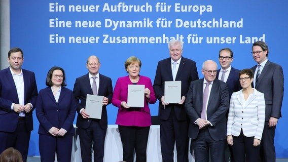 Olaf Scholz, Angela Merkel und Horst Seehofer halten den unterzeichneten Koalitionsvertrag in ihren Händen. Um sie herum stehen weitere Politikerinnen und Politiker aus der "Großen Koalition". © dpa - Bildfunk Foto: Michael Kappeler