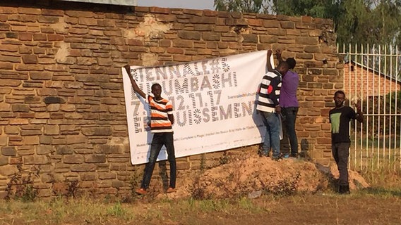 Einige Männer bringen ein Plakat an einer Mauer in Lubumbashi im Kongo an.  