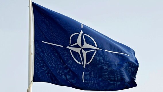 Eine blaue Fahne mit dem NATO-Logo weht draussen im Wind. © IMAGO/Panama Pictures Foto: Christoph Hardt