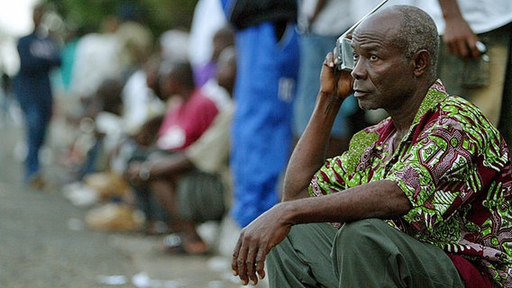 Ein Mann sitzt in Liberia am Straßenrand und hält sich ein kleines Radiogerät ans Ohr. © dpa picture alliance Foto: Nic Bothma