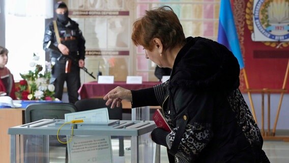 Eine Frau steckt bei einem der Scheinreferenden zum Anschluss ukrainischer Gebiete an Russland einen Wahlzettel in eine Urne. © Uncredited/AP/dpa 