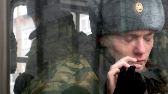 Ein junger Rekrut, der zum Militärdienst einberufen ist, weint, während er im Bus sitzt und eine weibliche Hand ihm an der Fensterscheibe zuwinkt (Archivbild). © epa/dpa Foto: Maxim Shipenkov