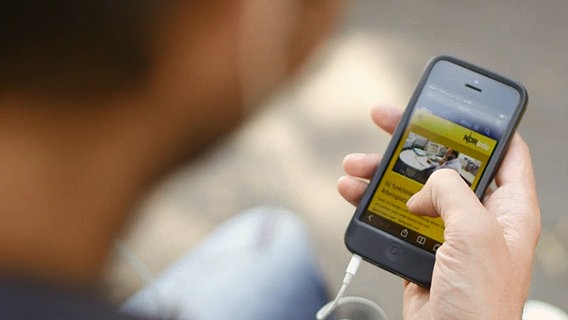 Ein Mann hat ein Smartphone in der Hand und hört NDR Info über die NDR Radio App. © Screenshot 