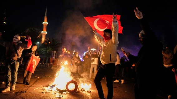 Ein Demonstrant schwenkt im nächtlichen Istanbul bei einer Demonstration gegen die Inhaftierung des Oppositionsführers Ekrem Imamoğlu eine türkische Fahne. © AP/dpa Foto: Emrah Gurel