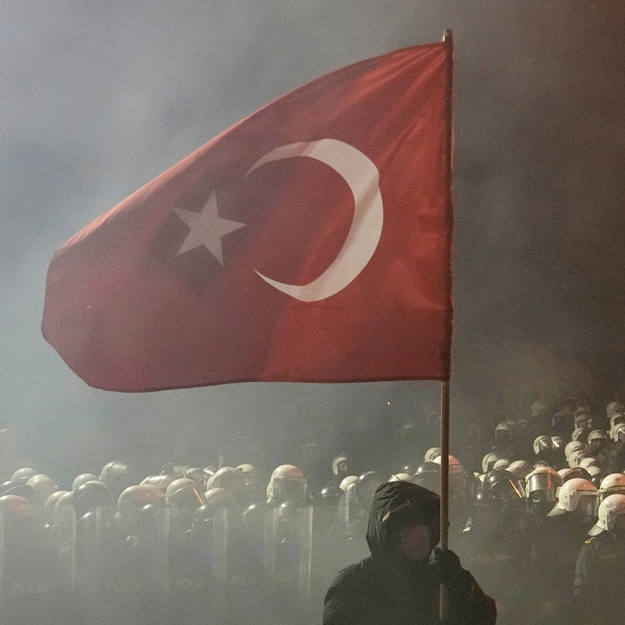 Ein Mann hält vor einem riesigen Polizeiaufgebot eine türkische Flagge während einer Demonstration gegen die Verhaftung des Istanbuler Bürgermeisters Imamoglu © AP/dpa Foto: Khalil Hamra