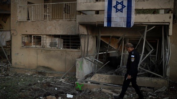 Ein israelischer Polizist läuft an einem durch eine Rakete zerstörten Gebäude in der nordisraelischen Stadt Karmiel vorbei. © picture alliance / ASSOCIATED PRESS | Leo Correa 