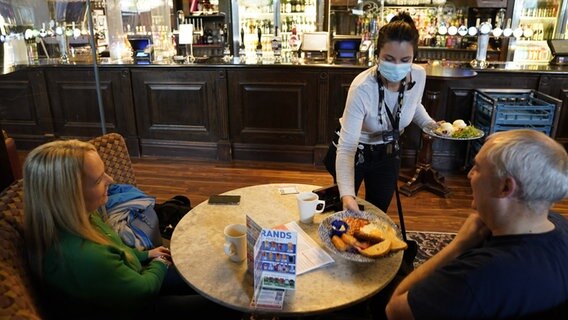 Großbritannien, Newcastle: Eine Kellnerin bringt zwei Gästen im Mile Castle Pub eine Mahlzeit an den Tisch.  